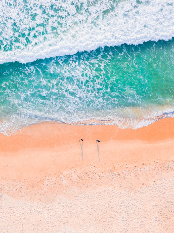 Stunning aerial shot of a sandy beach with turquoise ocean waves, capturing the natural beauty of the coastline.